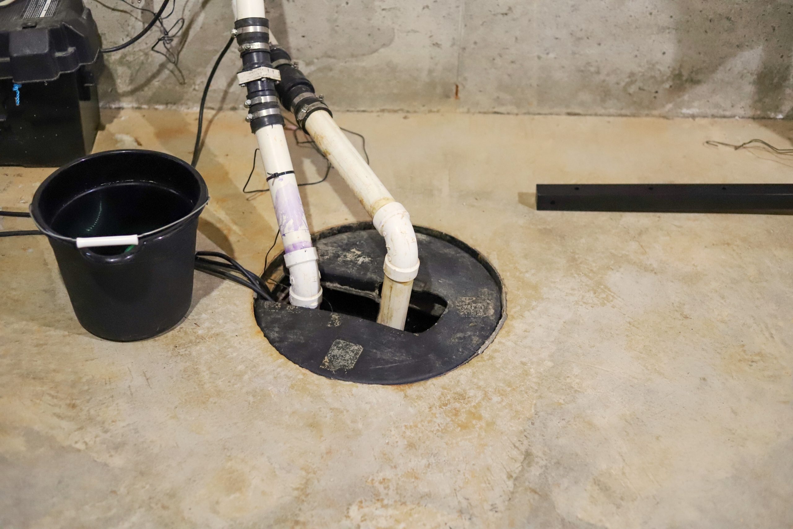 A sump pump in a basement with a bucket next to it